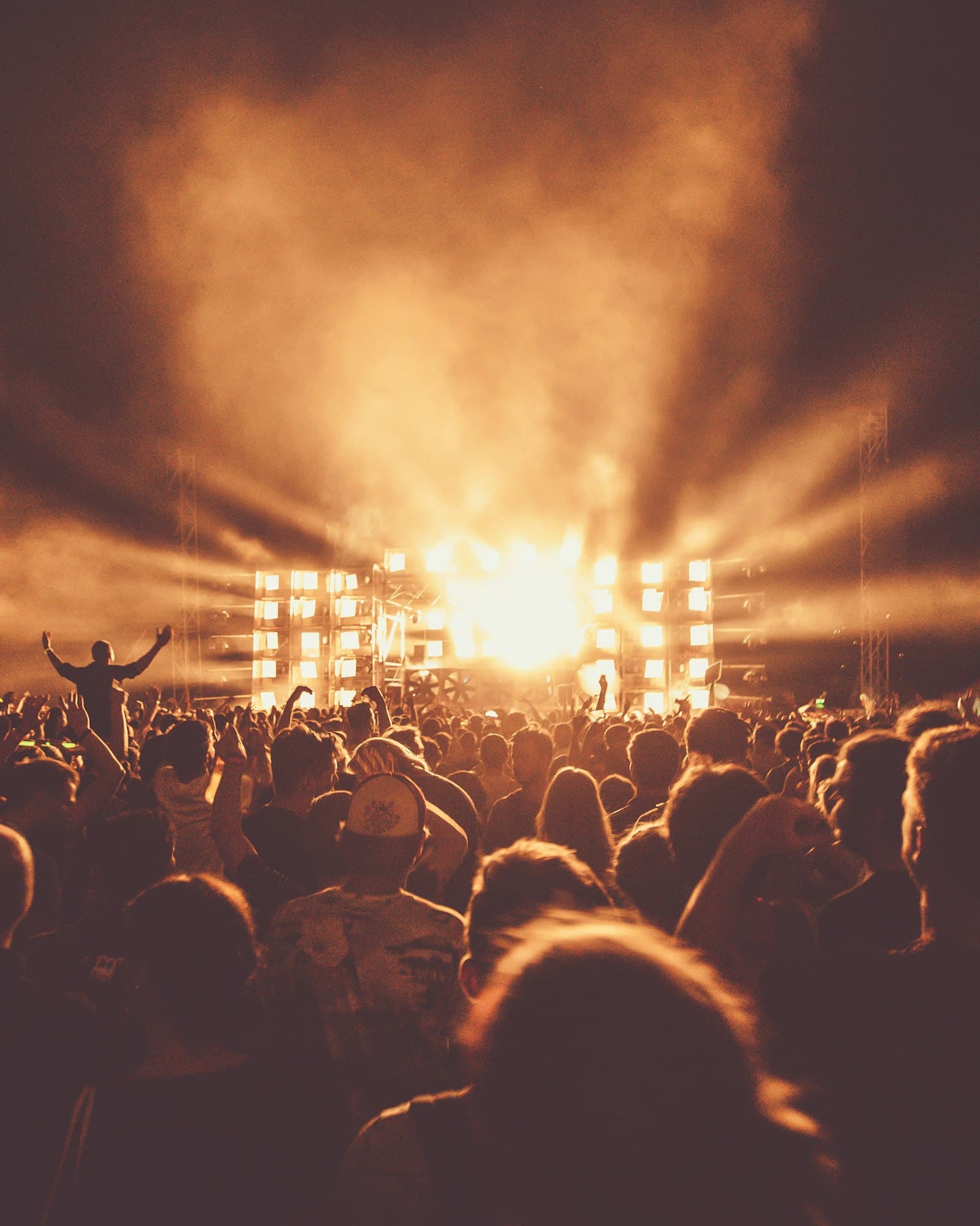 Sahne ışıklarının dumanda huzme yaptığı bir konser; önde kalabalığın silueti