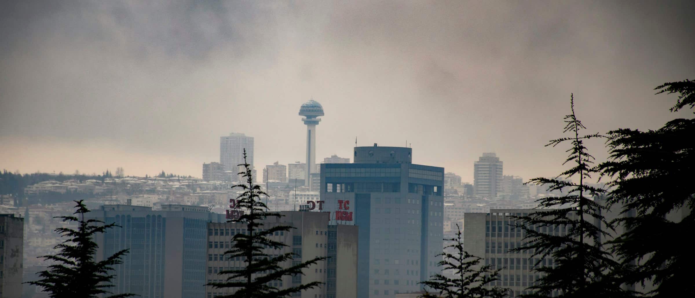 Sisli havada Ankara silueti; sırtın üzerinde Atakule, önde çam siluetleri